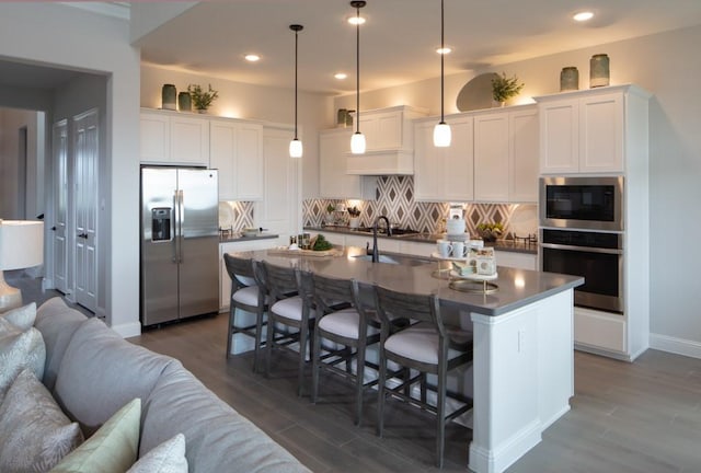 kitchen with a kitchen island with sink, hanging light fixtures, white cabinets, and appliances with stainless steel finishes