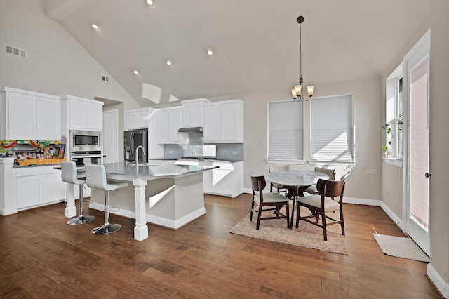 kitchen featuring dark wood-type flooring, white cabinetry, appliances with stainless steel finishes, light stone countertops, and a kitchen island with sink