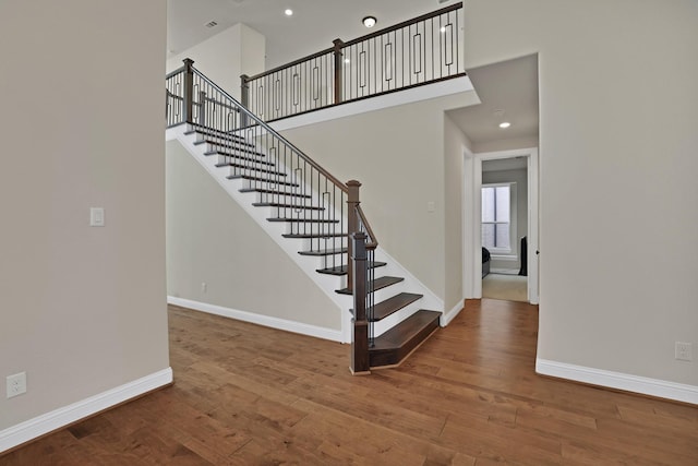 stairway with hardwood / wood-style flooring and a towering ceiling