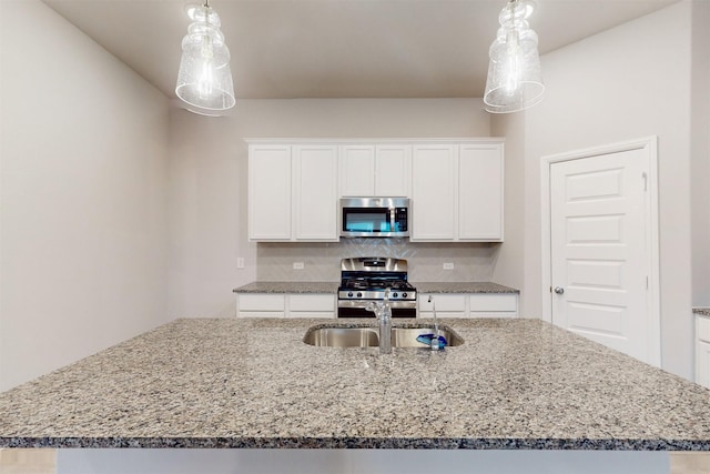 kitchen featuring appliances with stainless steel finishes, pendant lighting, white cabinetry, backsplash, and a kitchen island with sink