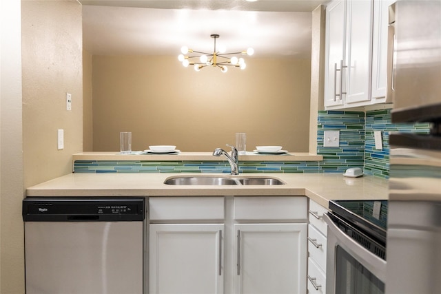 kitchen with appliances with stainless steel finishes, white cabinetry, sink, backsplash, and an inviting chandelier