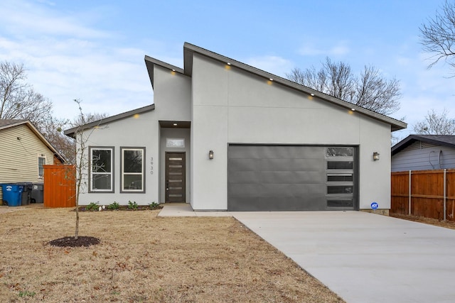 modern home with driveway, an attached garage, fence, and stucco siding