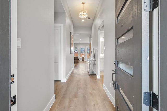 hallway with baseboards, visible vents, and light wood finished floors