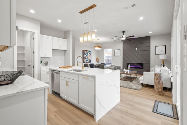 kitchen featuring a fireplace, light wood finished floors, white cabinets, a sink, and dishwasher