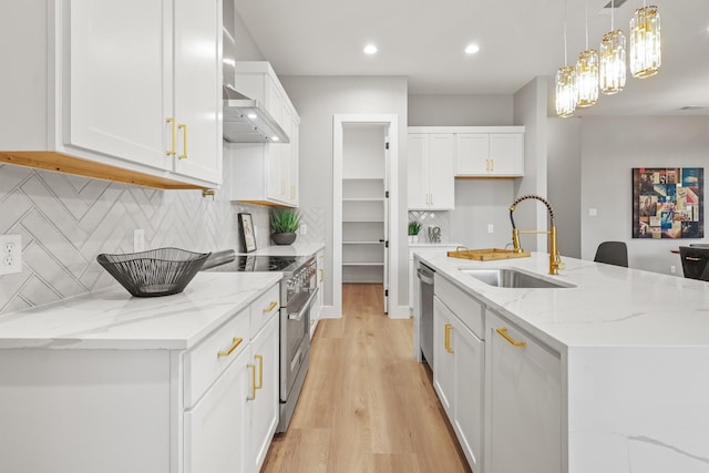 kitchen featuring stainless steel appliances, white cabinetry, a sink, wall chimney range hood, and light wood-type flooring