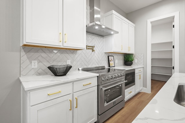 kitchen with white cabinets, stainless steel range, light stone countertops, and wall chimney range hood