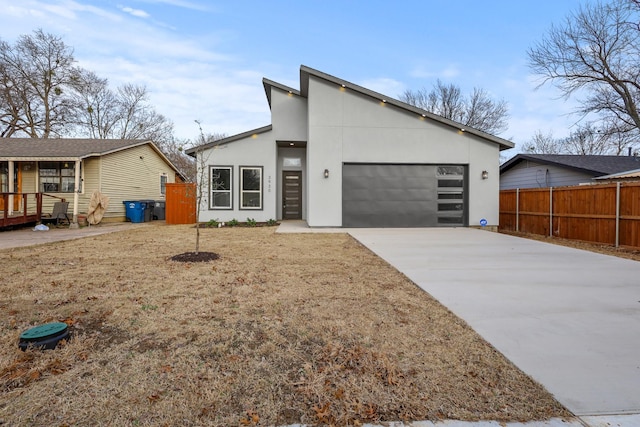 contemporary home with fence, driveway, an attached garage, and stucco siding