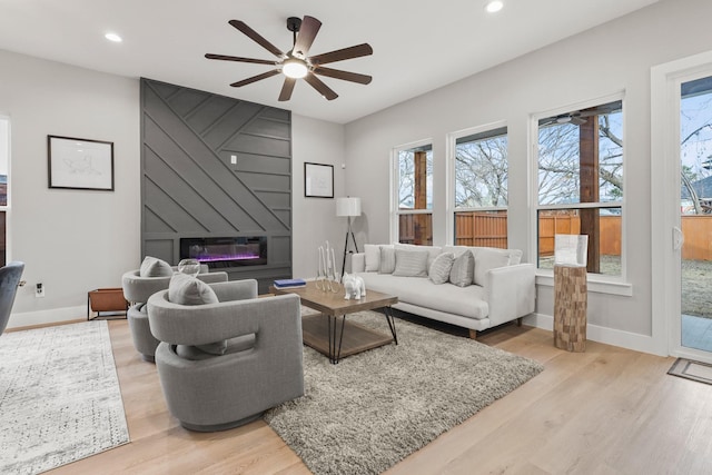 living room featuring a large fireplace, baseboards, wood finished floors, and recessed lighting