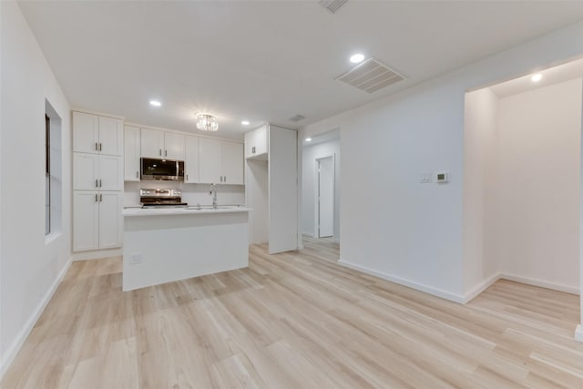 kitchen featuring white cabinetry, stainless steel appliances, light hardwood / wood-style floors, and a center island with sink