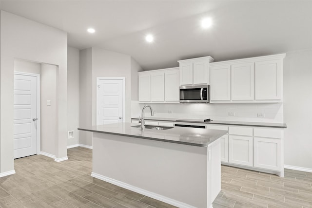 kitchen featuring white cabinets, stainless steel microwave, wood tiled floor, a kitchen island with sink, and a sink