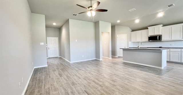 kitchen featuring light wood-style flooring, stainless steel microwave, ceiling fan, and visible vents