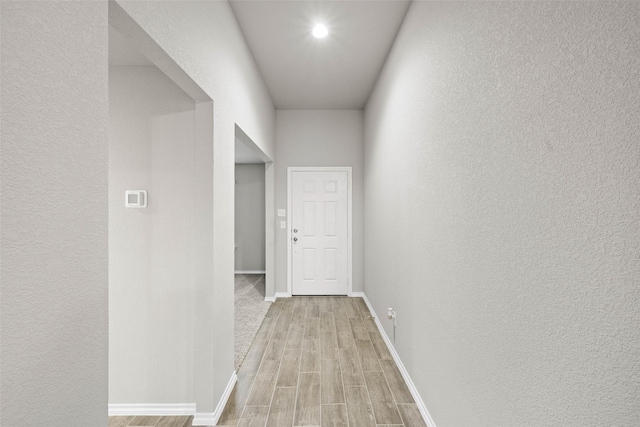 hallway featuring a textured wall, light wood-style flooring, and baseboards