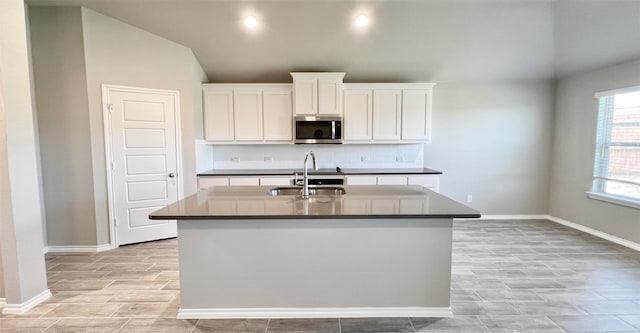 kitchen with decorative backsplash, dark countertops, stainless steel microwave, vaulted ceiling, and a sink