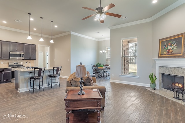 living room featuring hardwood / wood-style floors, crown molding, ceiling fan with notable chandelier, and a premium fireplace