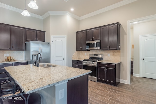 kitchen with decorative light fixtures, sink, dark brown cabinetry, stainless steel appliances, and a center island with sink