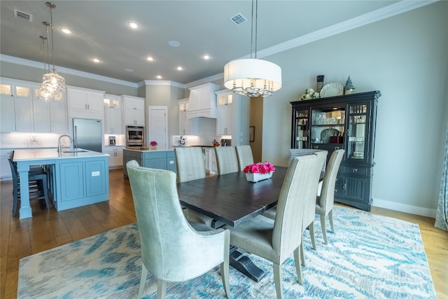 dining room featuring sink, crown molding, and light hardwood / wood-style flooring