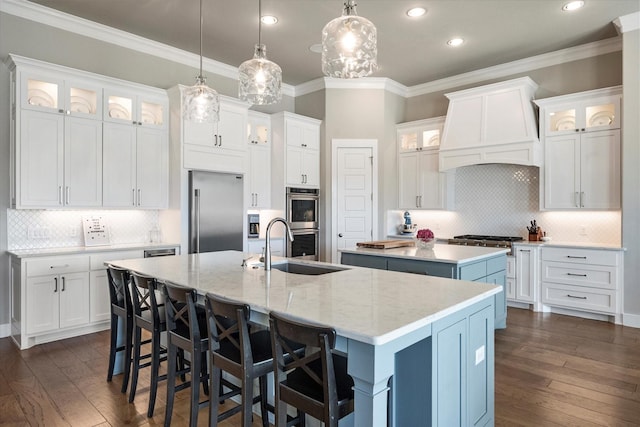 kitchen with white cabinets, a large island, custom range hood, appliances with stainless steel finishes, and a sink