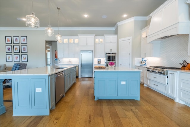 kitchen with custom exhaust hood, white cabinetry, a large island with sink, pendant lighting, and stainless steel appliances