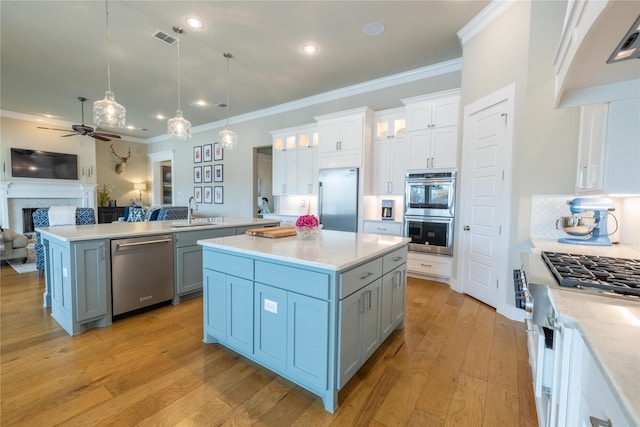 kitchen with sink, appliances with stainless steel finishes, hanging light fixtures, white cabinets, and a kitchen island