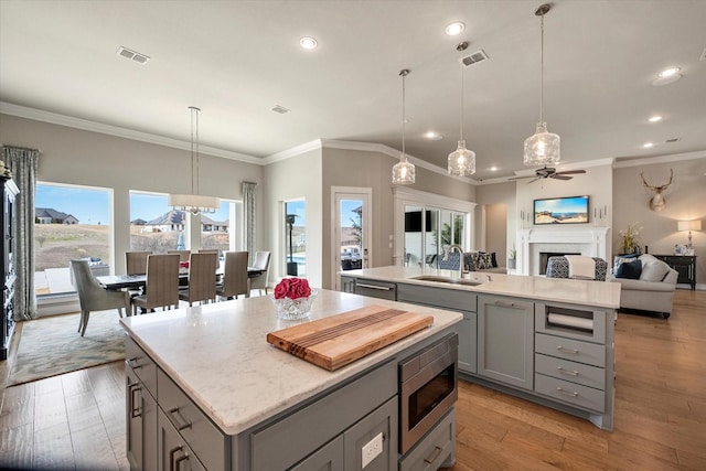 kitchen with a kitchen island with sink, stainless steel microwave, a sink, and gray cabinetry