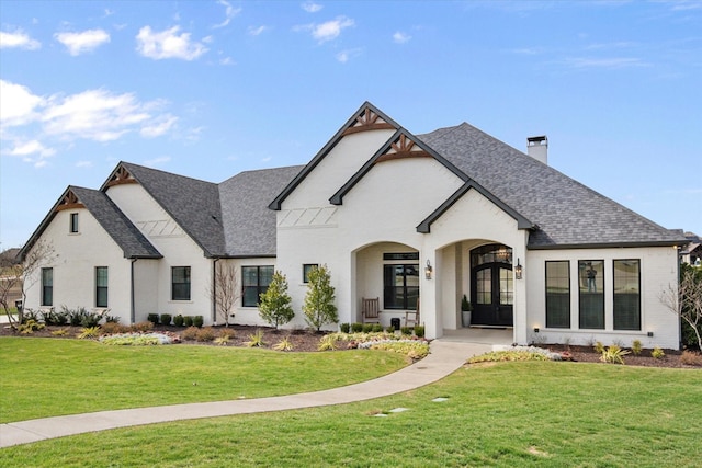 view of front of home featuring french doors, roof with shingles, a chimney, and a front lawn