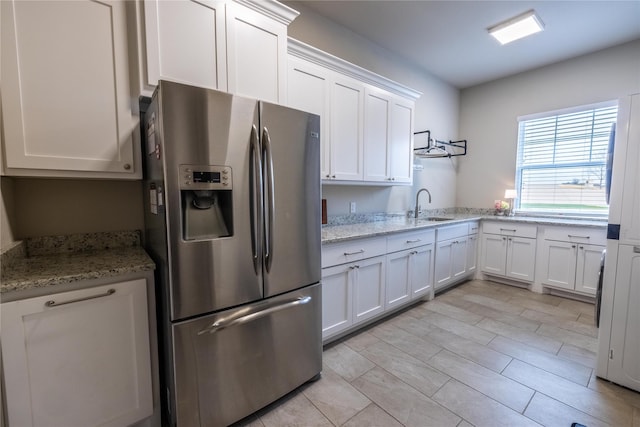 kitchen featuring stainless steel refrigerator with ice dispenser, sink, light stone counters, and white cabinets