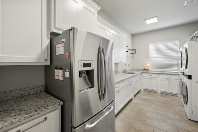 kitchen featuring a sink, white cabinets, stainless steel refrigerator with ice dispenser, light stone countertops, and stacked washer and clothes dryer