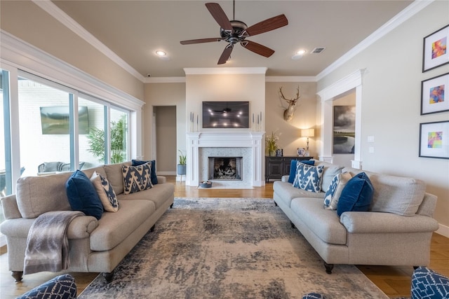 living room with hardwood / wood-style flooring, ornamental molding, ceiling fan, and a high end fireplace