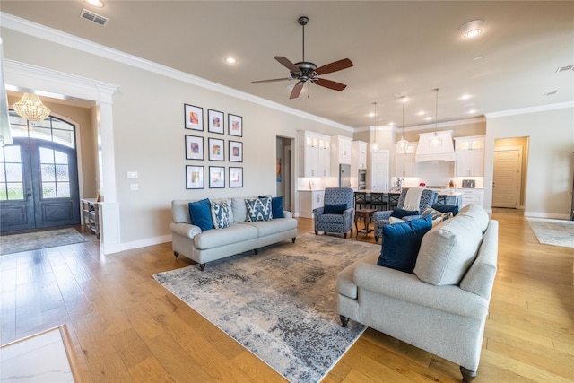 living room featuring french doors, ornamental molding, ceiling fan with notable chandelier, and light hardwood / wood-style flooring