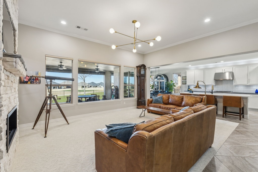 living room featuring crown molding, a stone fireplace, and a notable chandelier