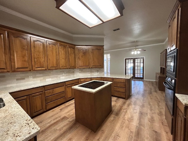 kitchen with light stone counters, ornamental molding, black appliances, a kitchen island, and kitchen peninsula