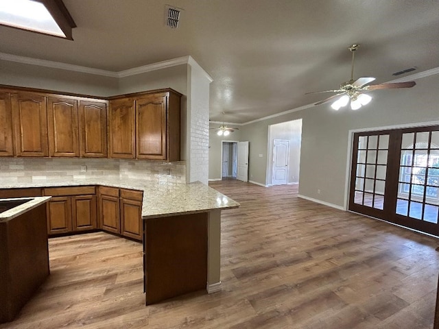 kitchen featuring light hardwood / wood-style flooring, ornamental molding, kitchen peninsula, light stone countertops, and backsplash