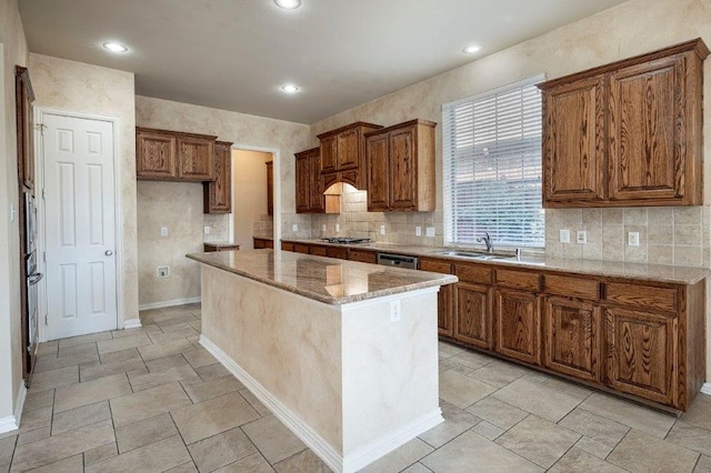 kitchen featuring sink, light stone counters, a center island, appliances with stainless steel finishes, and decorative backsplash