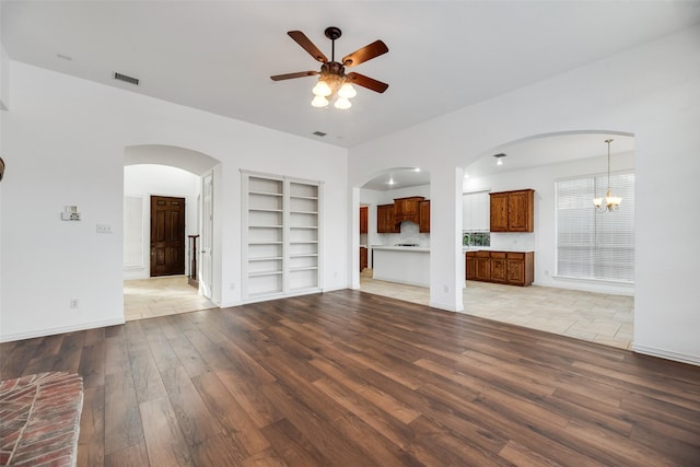 9328 Old Veranda Rd, Plano, TX 75024 - unfurnished living room featuring light wood-style floors, a ceiling fan, built in features, arched walkways, and a chandelier