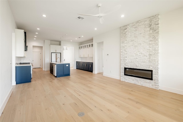 unfurnished living room featuring sink, a stone fireplace, light hardwood / wood-style flooring, and ceiling fan