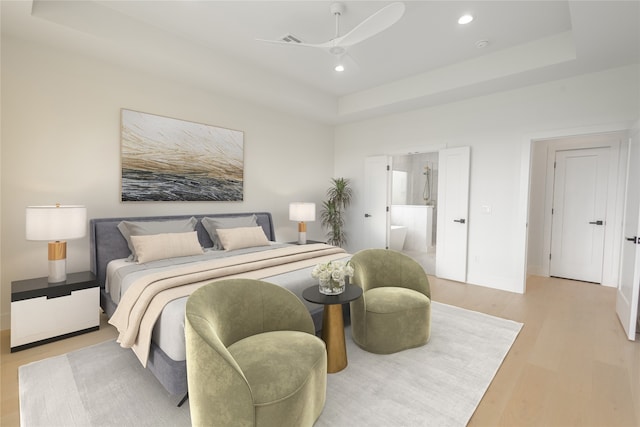 bedroom featuring a raised ceiling, ceiling fan, light hardwood / wood-style floors, and ensuite bath