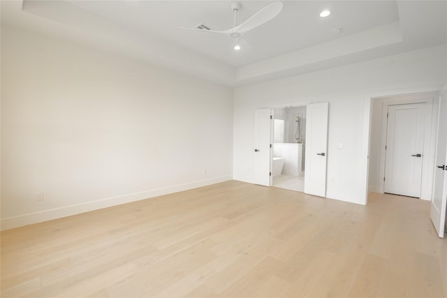 unfurnished bedroom with ceiling fan, ensuite bath, a tray ceiling, and light hardwood / wood-style floors