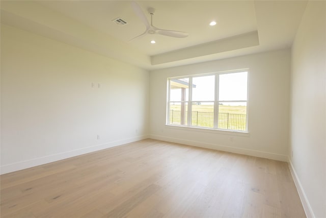 empty room featuring ceiling fan, a tray ceiling, and light hardwood / wood-style floors