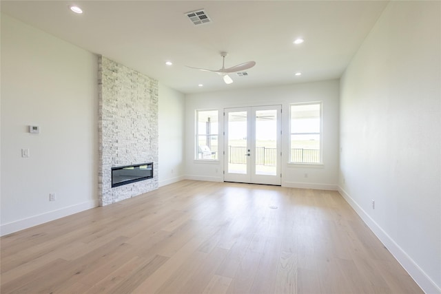 unfurnished living room featuring ceiling fan, a stone fireplace, light wood-type flooring, and french doors