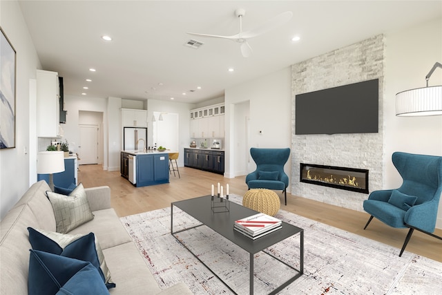 living room featuring ceiling fan, a fireplace, sink, and light hardwood / wood-style flooring