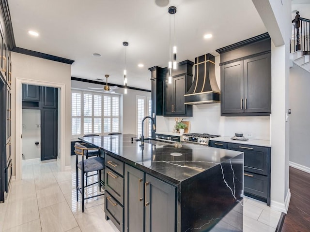 kitchen featuring pendant lighting, sink, crown molding, custom range hood, and a center island with sink