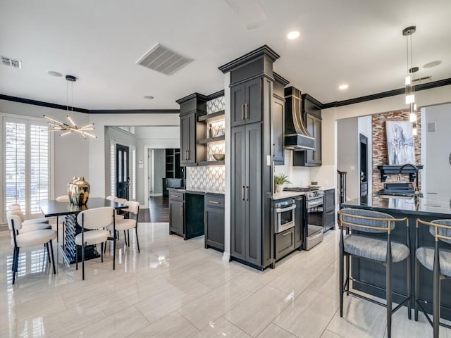 kitchen with a breakfast bar, premium range hood, ornamental molding, gas stove, and decorative light fixtures