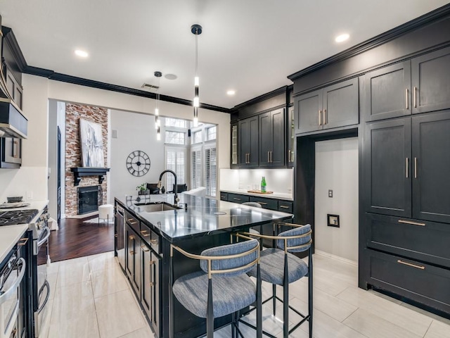 kitchen with a breakfast bar, sink, stainless steel gas stove, pendant lighting, and a kitchen island with sink