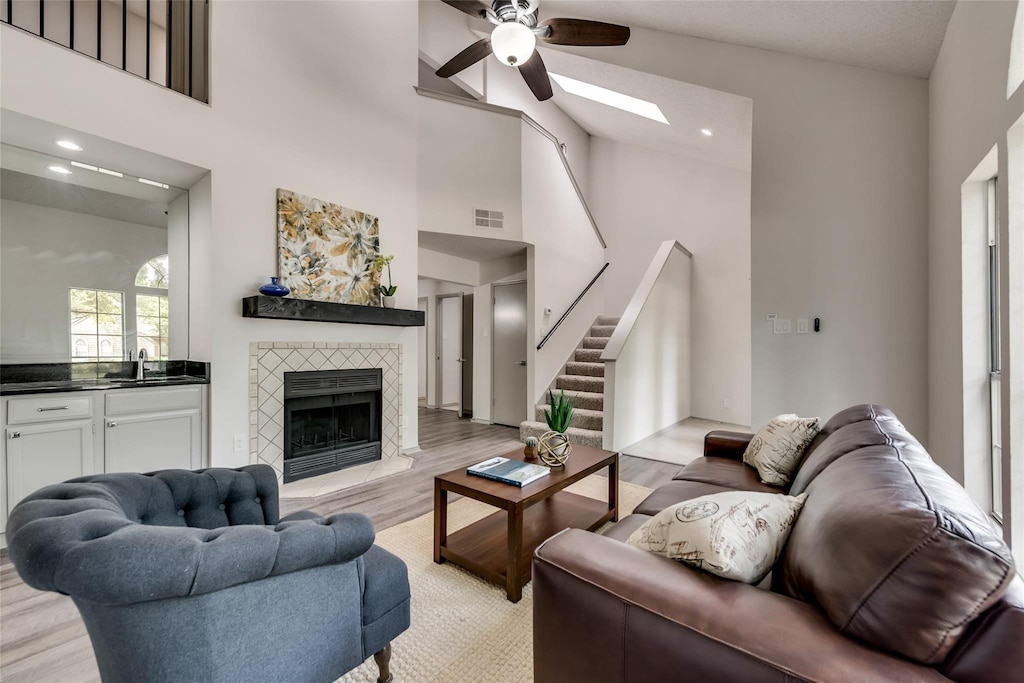 living area with visible vents, light wood-style floors, high vaulted ceiling, a tile fireplace, and stairs