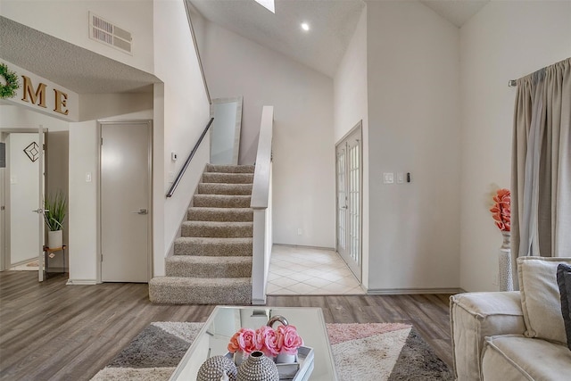 living room with high vaulted ceiling, light wood-type flooring, visible vents, and stairway