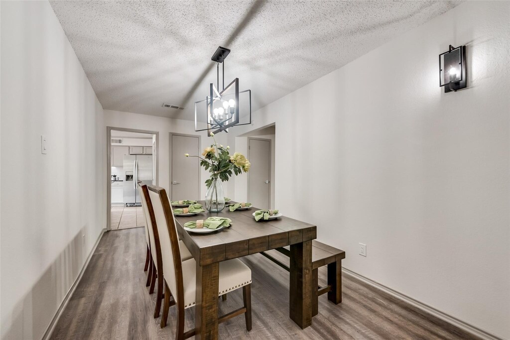 dining area featuring a notable chandelier, a textured ceiling, visible vents, and wood finished floors