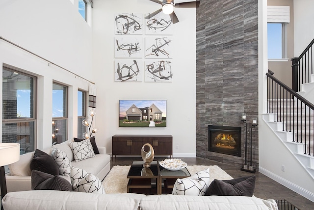 living room featuring ceiling fan, wood-type flooring, a tile fireplace, and a high ceiling