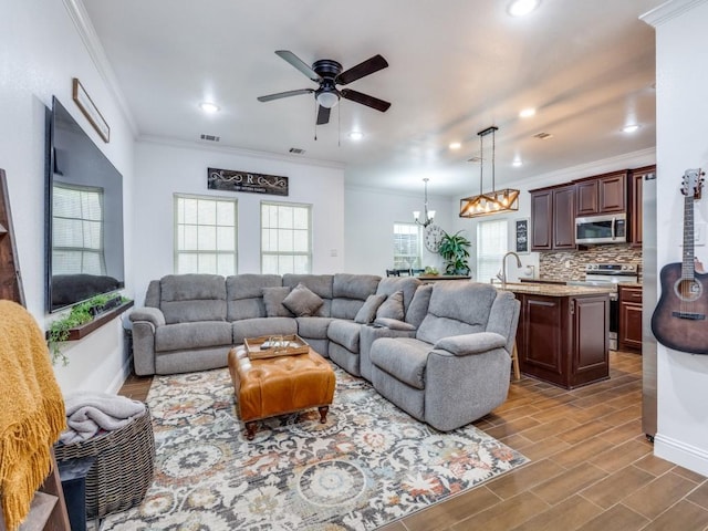 living room featuring sink, crown molding, and ceiling fan with notable chandelier