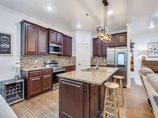 kitchen with appliances with stainless steel finishes, a breakfast bar, an island with sink, sink, and hanging light fixtures