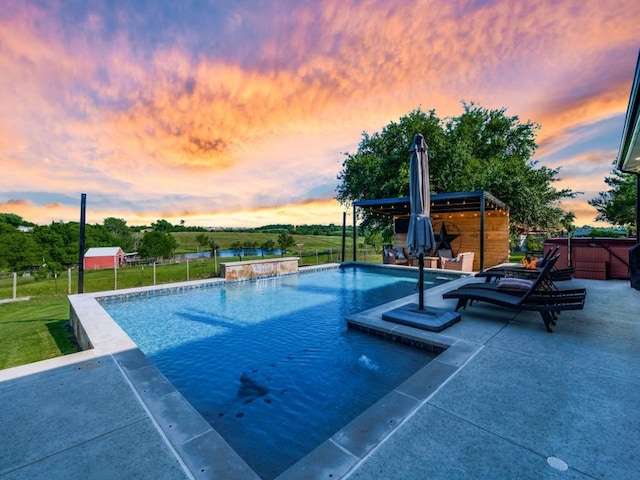 pool at dusk featuring a hot tub, pool water feature, a yard, and a patio area